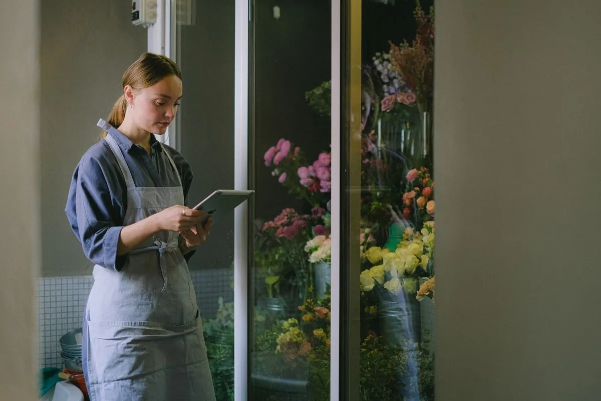 Florista consultando una tableta en su tienda, rodeada de flores