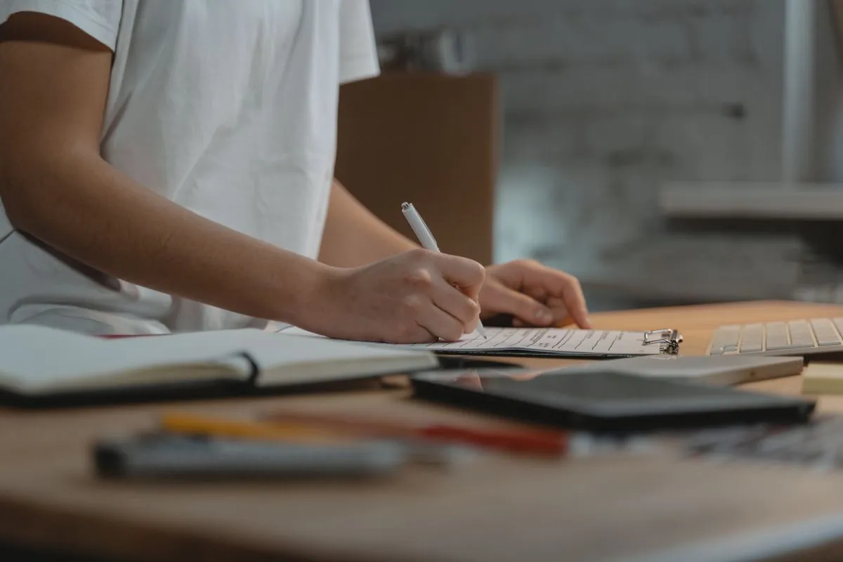 Persona revisando y anotando una tarea en papel sobre la mesa de trabajo