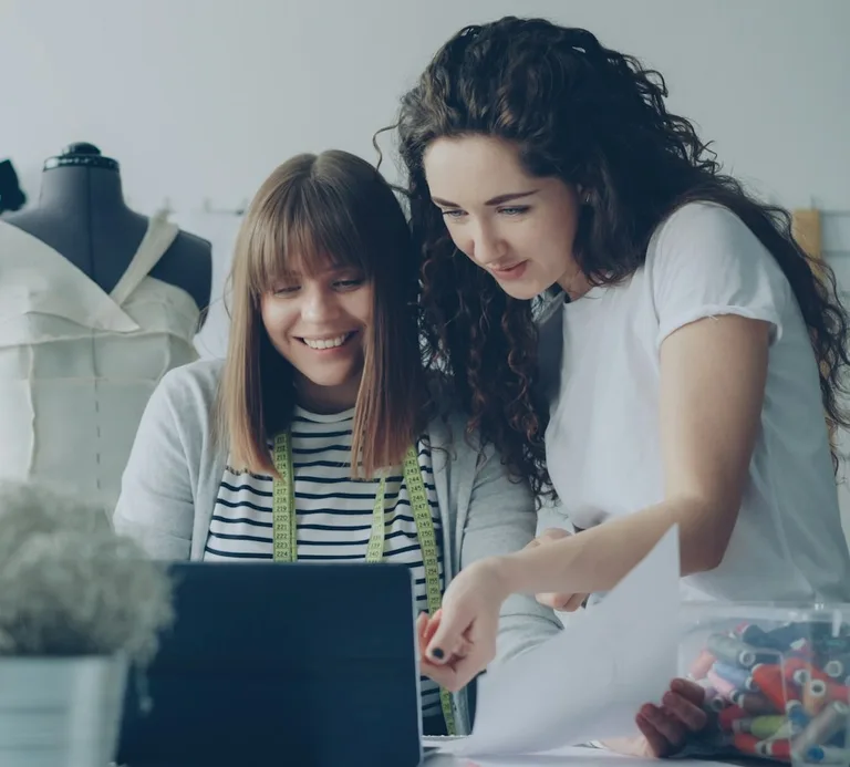 Dos mujeres revisan juntas un portátil en su taller de costura